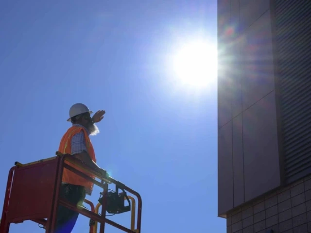 a construction worker standing on a lift near a building in the direct midday sun