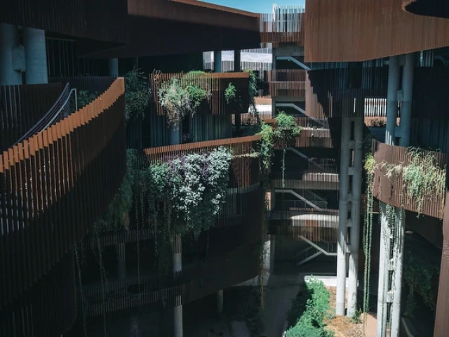 Interior view of the ENR2 Building’s canyon-like courtyard, with rust-colored fins, open-air walkways, and terraces covered in hanging vines and greenery.