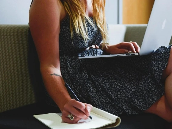 a woman writing with a notebook and a laptop