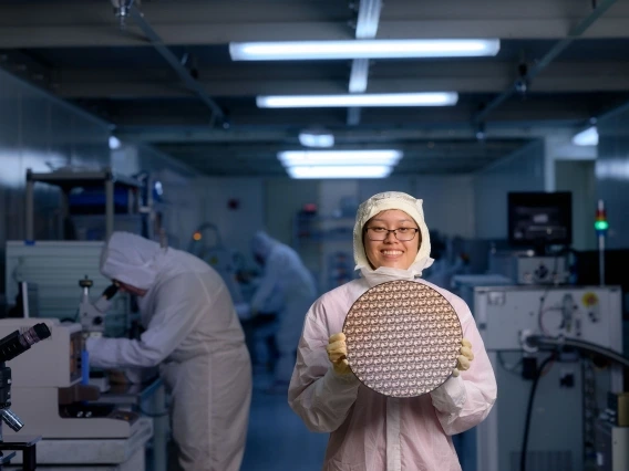 a person in a lab suit holding a test wafer while standing in a lab