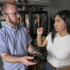 Matthew Briggs talks with Ruth Salazar while holding an adaptive foot pedal in a lab with 3D printers in the background