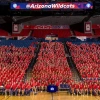 Hundreds of University of Arizona student-athletes wearing red shirts sit together in the shape of a large block “A” inside McKale Memorial Center during the Arizona Athletics welcome back BBQ. An American flag hangs above, and a scoreboard displays the @ArizonaWildcats handle.