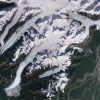 A satellite image of glaciers in Alaska shows white flows of ice surrounded by dark green mountain ridges